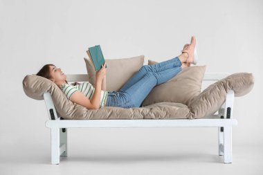 Genç bir kadın, renkli arka planda modern koltukta kitap okuyor.