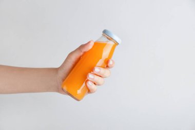 Hafif arka planda meyve suyu şişesi olan bir kadın eli.