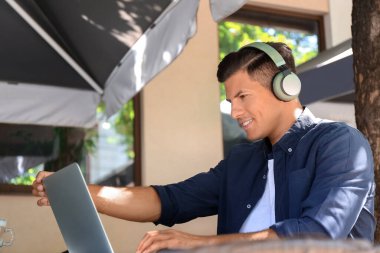 Kulaklıklı bir adam açık kafede dizüstü bilgisayarla çalışıyor.