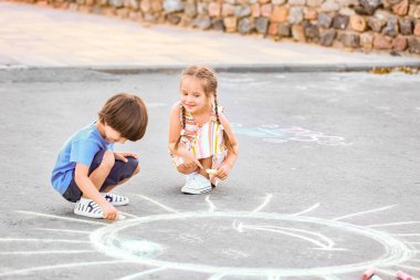 Küçük çocuklar asfalta tebeşirle resim çiziyor.