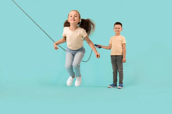 Cute little children jumping rope against color background