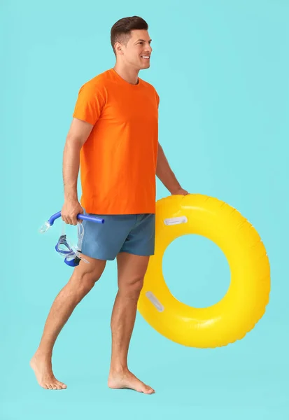 Young man with inflatable ring, snorkeling mask and tube on color background