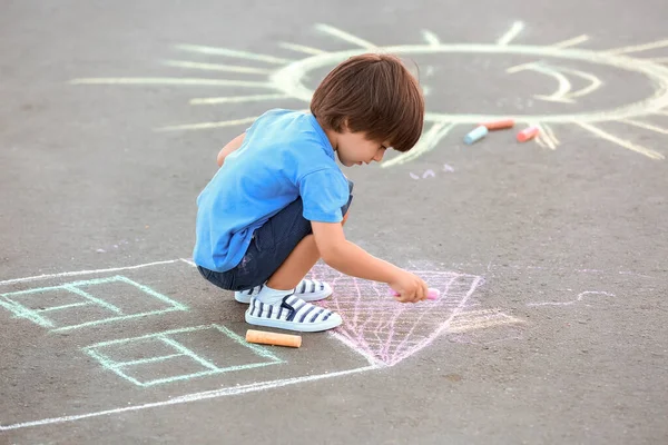 Little boy drawing with chalk on asphalt