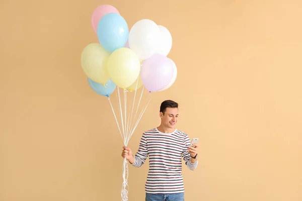 Young man with balloons and mobile phone on color background