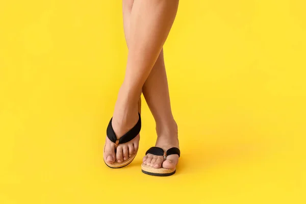 Legs of young woman in flip-flops on color background
