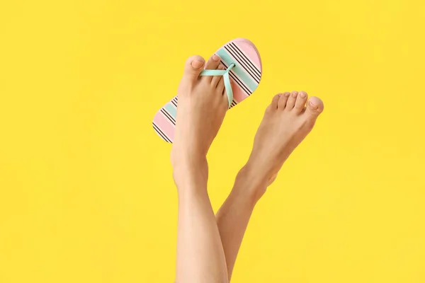 Legs of young woman in flip-flops on color background