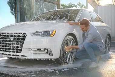 Adam dışarıda arabasını yıkıyor.