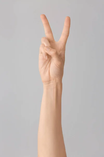 Hand showing letter V on grey background. Sign language alphabet