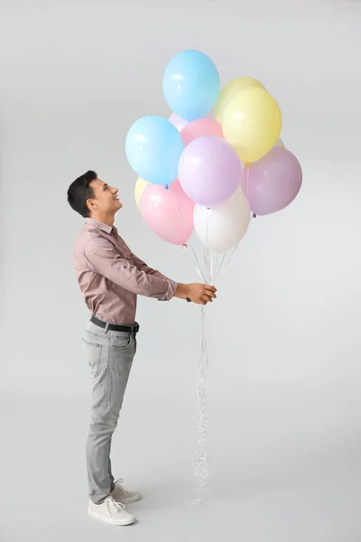 Young man with balloons on grey background