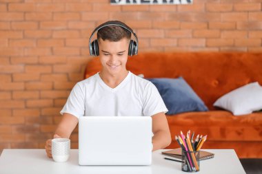 Evde müzik dinleyen dizüstü bilgisayarı olan genç bir çocuk.