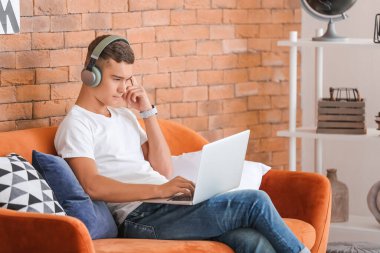Evde müzik dinleyen dizüstü bilgisayarı olan genç bir çocuk.