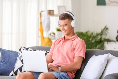 Evde müzik dinleyen dizüstü bilgisayarı olan genç bir çocuk.