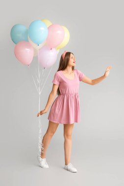 Gri arka planda balonları olan genç bir kadın.
