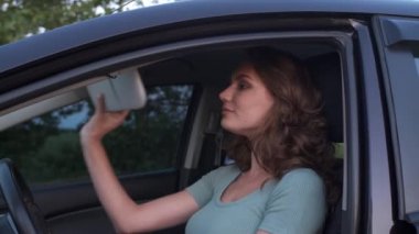 Genç bir kadın arabada otururken dikiz aynasında kendini güzelleştiriyor.