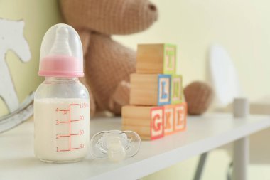 Bebek için bir şişe süt, emzik ve oyuncaklar masada.