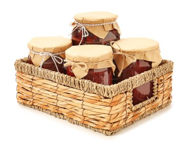 Beyaz arka planda reçel kavanozları olan hasır sepet.