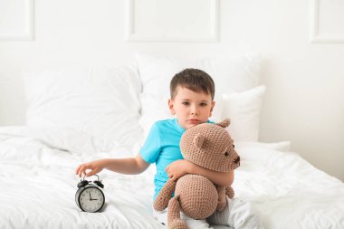 Yatak odasında çalar saat olan uyku bozukluğu çeken küçük bir çocuk.