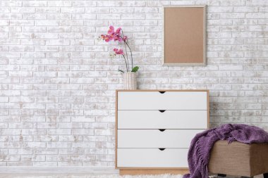 Odada tuğla duvarın yanında puf olan modern çekmeceler.