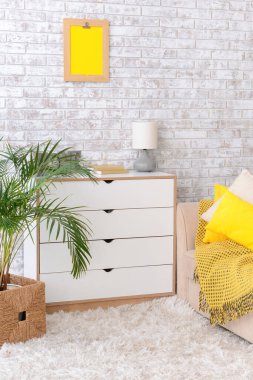 Oda duvarının yanında kanepe ve çiçek bulunan modern çekmeceler.