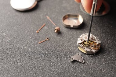 Saatçi masadaki kırık saati tamir ediyor, kapatıyor.