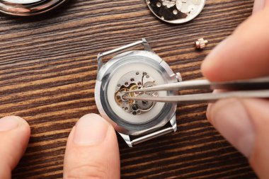 Saatçi masadaki kırık saati tamir ediyor, kapatıyor.