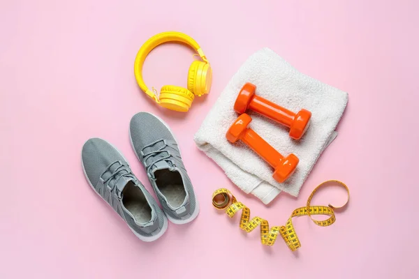 Sportive shoes, dumbbells, towel, measuring tape and headphones on color background