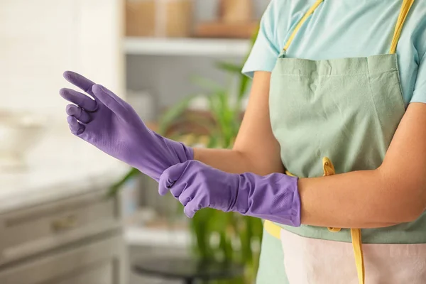 Woman putting on rubber gloves in kitchen
