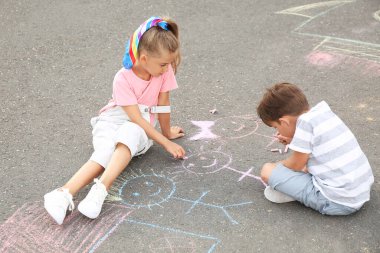 Küçük çocuklar asfalta tebeşirle resim çiziyor.
