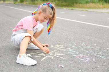 Küçük kız asfalta tebeşir çiziyor.