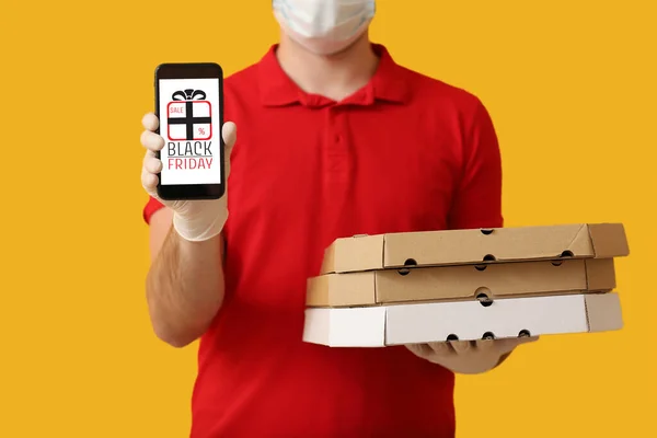 Male courier of food delivery company in medical mask and with mobile phone on color background. Black Friday sale