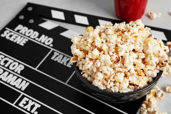 Popcorn and movie clapper on light background
