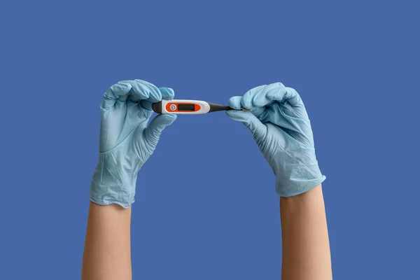 Hands of doctor with thermometer on color background