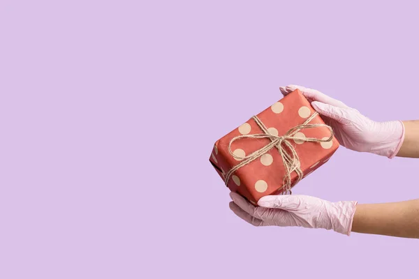 Hands in protective gloves and with gift box on color background