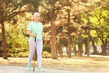 Olgun bir kadın, dışarıda sırıklarla yürüyor.