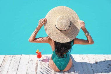 Tropikal tatil köyünde yüzme havuzunun yanında kokteyl içen güzel genç bir kadın.