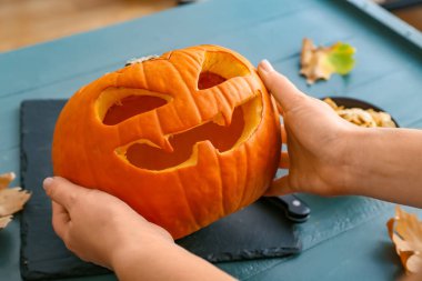 Cadılar Bayramı 'nda masada oyulmuş balkabağı olan kadın.
