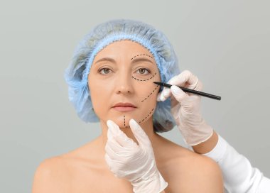 Plastik cerrah, gri arka planda kadınların yüzüne izler yapıştırıyor.