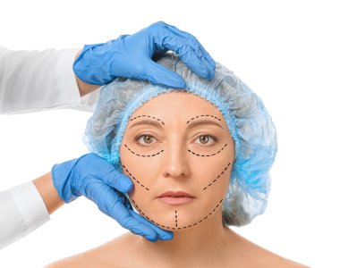 Plastik cerrah beyaz arka planda kadının yüzünü inceliyor.