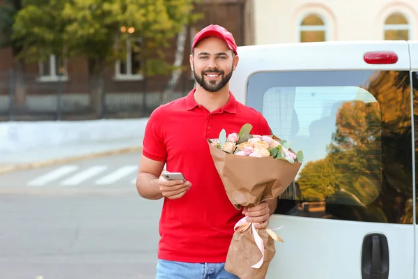 美しい花の花束と屋外で車の近くの携帯電話を持つ配達の男 — ストック写真