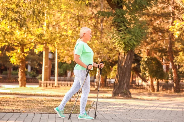 Olgun bir kadın, dışarıda sırıklarla yürüyor.