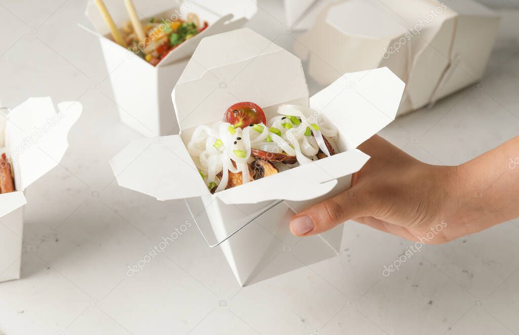 Woman with tasty rice noodles in box on light background