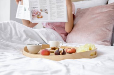 Genç bir kadının yatağında lezzetli bir kahvaltı tepsisi.