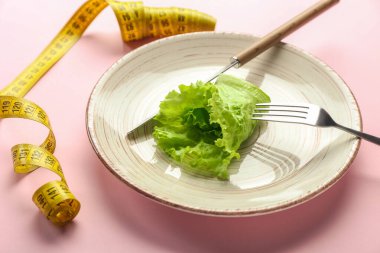 Çatal bıçaklı tabak, salata ve renkli arka planda mezura. İştahsızlık kavramı