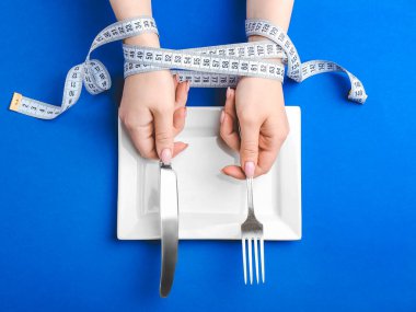 Ölçüm bandı, boş tabak ve renkli çatal bıçak takımı olan kadın elleri. İştahsızlık kavramı