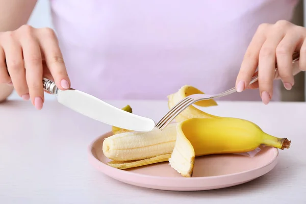 Woman eating banana at table. Concept of anorexia