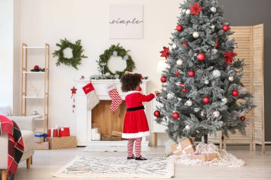Noel Baba kostümlü tatlı Afro-Amerikalı kız Noel ağacını evde süslüyor.