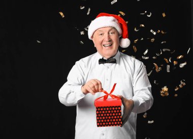 Karanlık arka planda Noel hediyesi olan yaşlı bir adam.