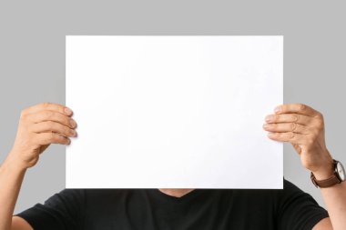 Gri arkaplanda boş kağıt sayfası olan adam.