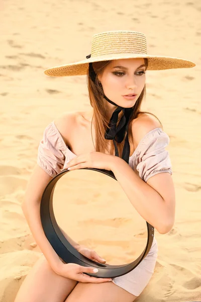 Beautiful fashionable young woman with mirror in desert
