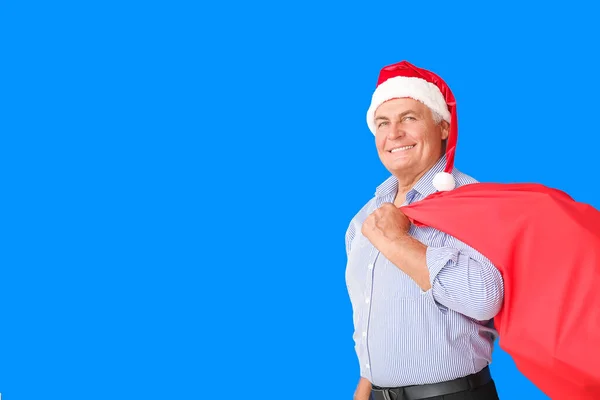 Elderly man in Santa hat and with bag on color background